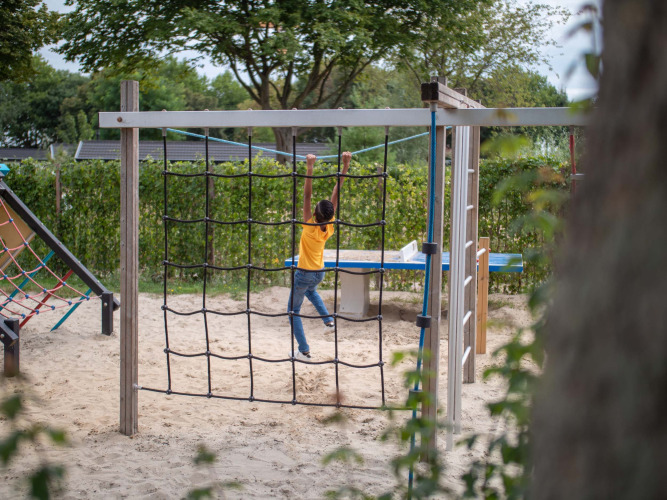 A child playing on a playground climbing net at Recreatiepark het Esmeer in Gelderland, Netherlands.