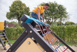 Junge im gelben Shirt klettert auf einem Spielplatz im Recreatiepark het Esmeer, Gelderland, Niederlande.