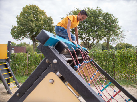Ragazzo con maglietta gialla che scala un parco giochi al Recreatiepark het Esmeer, Gelderland, Paesi Bassi.