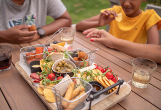 Familie genießt eine Platte mit Snacks im Freien auf einem Holztisch im Recreatiepark het Esmeer, Gelderland.