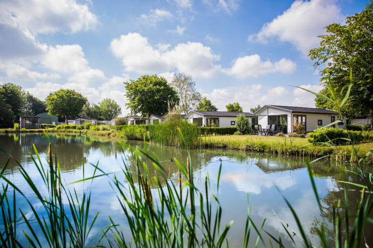 Holiday cottages by a lake at Recreatiepark het Esmeer in Gelderland, surrounded by greenery and clear sky.
