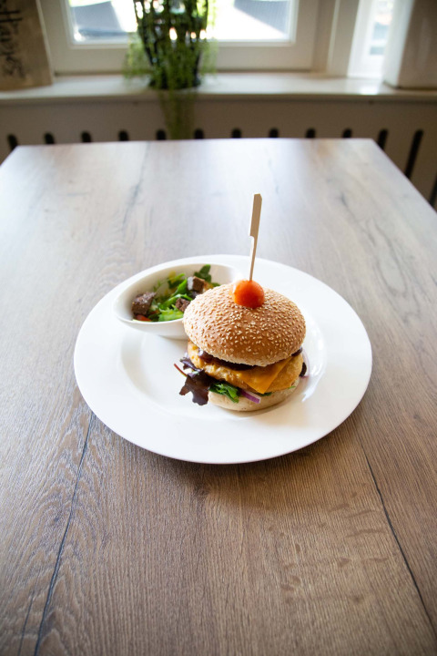 En cheeseburger med salat serveres på en hvid tallerken på et træbord i et lyst rum i Gelderland.