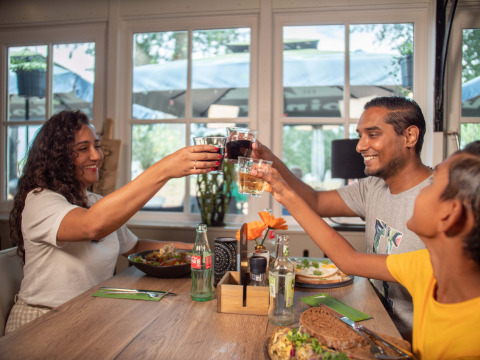 A happy family enjoys a meal and toasts with drinks at Recreatiepark het Esmeer, Gelderland, Netherlands.