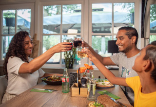 Een blije familie geniet van een maaltijd en brengt een toast uit in Recreatiepark het Esmeer, Gelderland.
