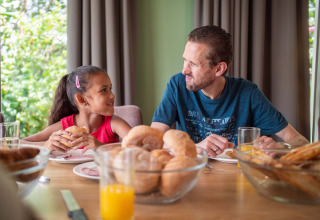 Padre e figlia sorridono durante la colazione presso Résidence Lichtenvoorde, parco vacanze nei Paesi Bassi.