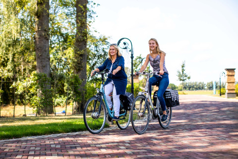 Twee vrouwen fietsen samen in het vakantiepark Résidence Lichtenvoorde in Gelderland, Nederland, in de zon.