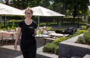 En smilende servitrice serverer drikkevarer på udendørs terrasse i Résidence Lichtenvoorde, Gelderland.