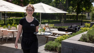 Una camarera sonriente sirve bebidas en la terraza exterior de Résidence Lichtenvoorde, Gelderland.