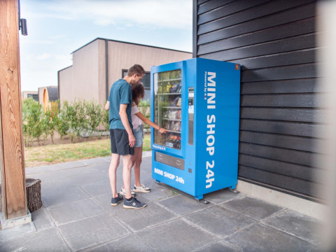 Dos personas utilizan una máquina expendedora azul 24h al aire libre en Résidence Lichtenvoorde, Gelderland.