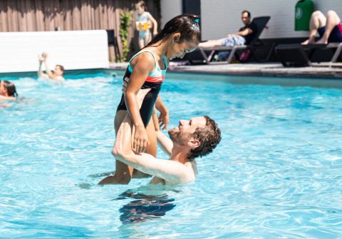Uomo solleva una bambina sorridente in costume nella piscina all'aperto di Résidence de Leuvert, Brabante Settentrionale.