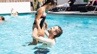 Man lifts smiling girl in swimsuit at outdoor pool in Résidence de Leuvert holiday park, North-Brabant, Netherlands.