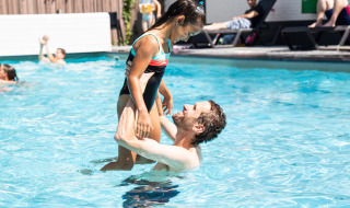 Hombre levanta a una niña sonriente en bañador en la piscina exterior de Résidence de Leuvert, Brabante Septentrional.