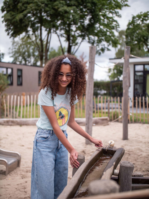 Mädchen spielt an einem Wasserlauf auf dem Spielplatz im Ferienpark Résidence de Leuvert, Nordbrabant.
