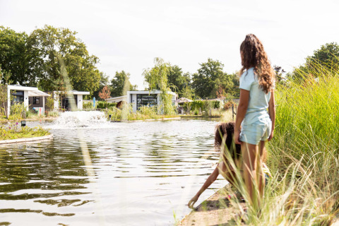 Two children play by the water’s edge at Résidence de Leuvert holiday park with lodges in North Brabant, Netherlands.