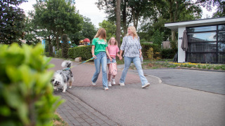 Family walking their dog at Résidence de Leuvert holiday park in North-Brabant, Netherlands, enjoying nature.