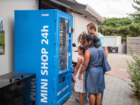 Familie benutzt blauen 24h-Minishop-Automaten im Ferienpark Résidence de Leuvert, Nordbrabant, Niederlande.