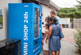 Familie benutzt blauen 24h-Minishop-Automaten im Ferienpark Résidence de Leuvert, Nordbrabant, Niederlande.