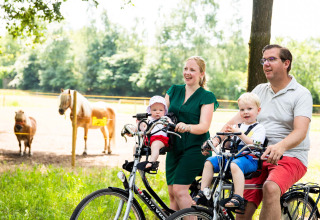Familie fährt mit Kindern auf Fahrrädern an Ponys vorbei im Ferienpark Résidence de Leuvert, Nordbrabant.