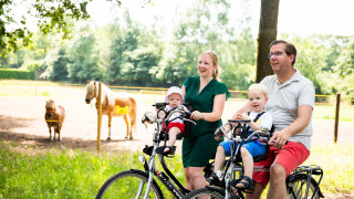 Family cycling with young children past ponies at Résidence de Leuvert holiday park in North-Brabant, Netherlands.