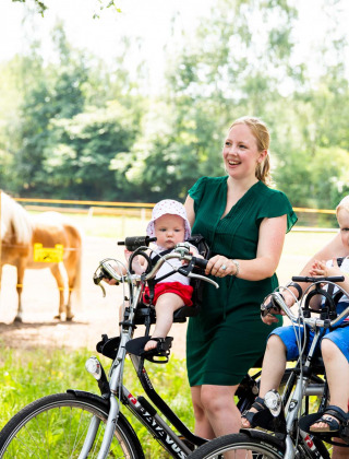 Familia en bicicleta con niños pequeños junto a ponis en Résidence de Leuvert, un parque vacacional en Brabante Septentrional.