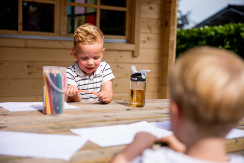 Zwei Kinder malen draußen am Holztisch mit Buntstiften im Ferienpark Résidence de Leuvert, Nordbrabant.
