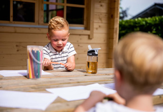 Zwei Kinder malen draußen am Holztisch mit Buntstiften im Ferienpark Résidence de Leuvert, Nordbrabant.