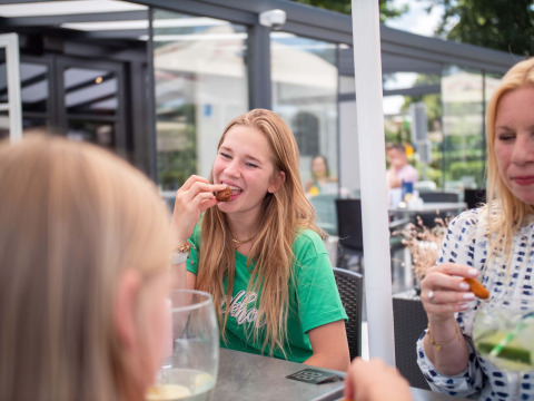Junge Frauen essen gemeinsam draußen im Résidence de Leuvert Ferienpark in Nordbrabant, Niederlande.