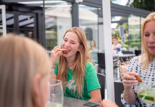 Junge Frauen essen gemeinsam draußen im Résidence de Leuvert Ferienpark in Nordbrabant, Niederlande.