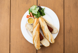 Two baguettes with meat croquettes, mixed greens, and mustard on a white plate on a wooden table.