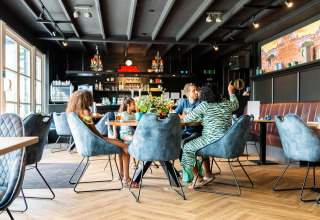 En familie nyder en frokost sammen i en moderne restaurant på ferieparken Résidence de Leuvert i Holland.