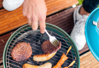 Iemand barbecuet hamburgers, worsten en kipspiesjes op een klein barbecuetoestel bij Landgoed de Scheleberg.