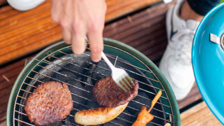 Iemand barbecuet hamburgers, worsten en kipspiesjes op een kleine barbecue bij Landgoed de Scheleberg.
