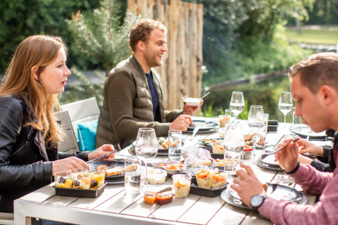 Menschen essen gemeinsam an einem Tisch im Freien bei Landgoed de Scheleberg, Gelderland, Niederlande.