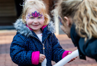 Bambina con il viso dipinto e giacca sorridente all'aperto a Landgoed de Scheleberg, Gelderland.