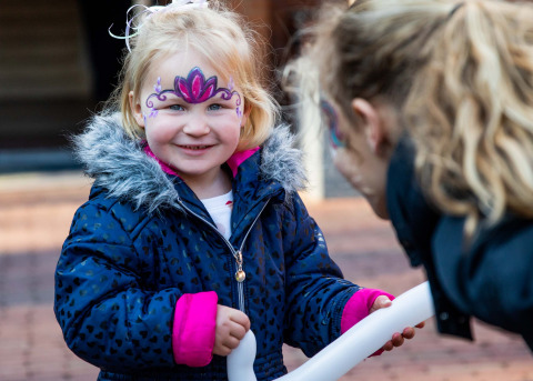 Klein meisje met schmink en winterjas lacht buiten bij Landgoed de Scheleberg in Gelderland.