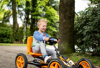 Dreng kører på pedalbil i ferieparken Landgoed de Scheleberg i Gelderland, Holland, omgivet af natur.