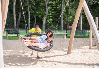 Mann schaukelt zwei Kinder auf einer Nestschaukel im Ferienpark Landgoed de Scheleberg, Gelderland.