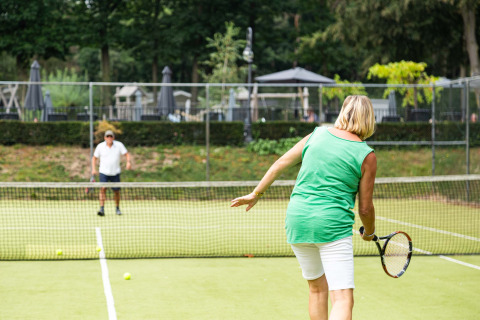 Two people playing tennis on a green court at Landgoed de Scheleberg holiday park in Gelderland.