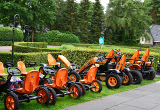 Several orange pedal go-karts are parked on the grass at Landgoed de Scheleberg, Gelderland, Netherlands.
