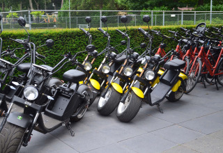 Row of electric scooters and bicycles parked outside at Landgoed de Scheleberg park in Gelderland, Netherlands.