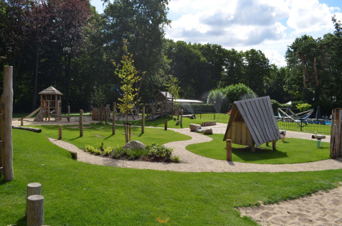 Speeltuin met houten hutten en gras op Landgoed de Scheleberg vakantiepark in Gelderland, Nederland.