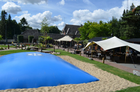 Außenbereich im Ferienpark Landgoed de Scheleberg in Gelderland, Niederlande, mit Hüpfkissen und Sitzplätzen.