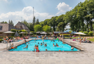 Piscina al aire libre llena de huéspedes de vacaciones, niños y adultos, rodeada de tumbonas y sombrillas.