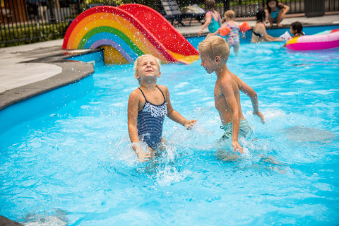 Kinder spielen und planschen im Schwimmbad mit einer bunten Regenbogenrutsche im Landgoed de Scheleberg.