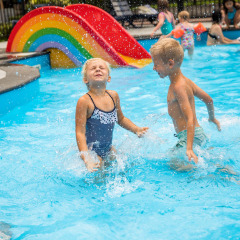 Kinderen spetteren en spelen in het zwembad met een kleurrijke regenboogglijbaan op Landgoed de Scheleberg.