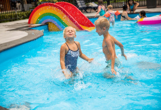 Kinderen spetteren en spelen in het zwembad met een kleurrijke regenboogglijbaan op Landgoed de Scheleberg.