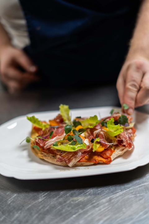 Un chef présente un plat gourmet avec jambon, salade et herbes à Landgoed de Scheleberg, Gelderland.