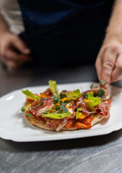 Een chef serveert een gourmetgerecht met ham, sla en kruiden bij Landgoed de Scheleberg in Gelderland.