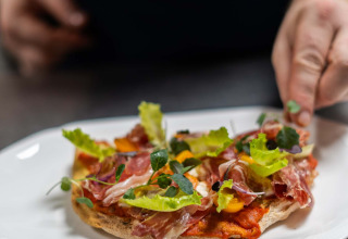 Uno chef presenta un piatto gourmet con prosciutto, lattuga ed erbe a Landgoed de Scheleberg, Gelderland.