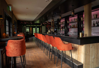 Moderne Bar mit orangefarbenen Stühlen in Landgoed de Scheleberg, einem Ferienpark in Gelderland, Niederlande.